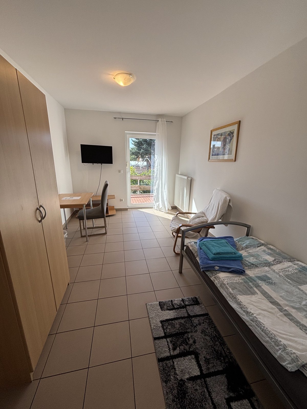 Möbliertes Einzelzimmer mit Bett, Schrank, Schreibtisch und Balkontür