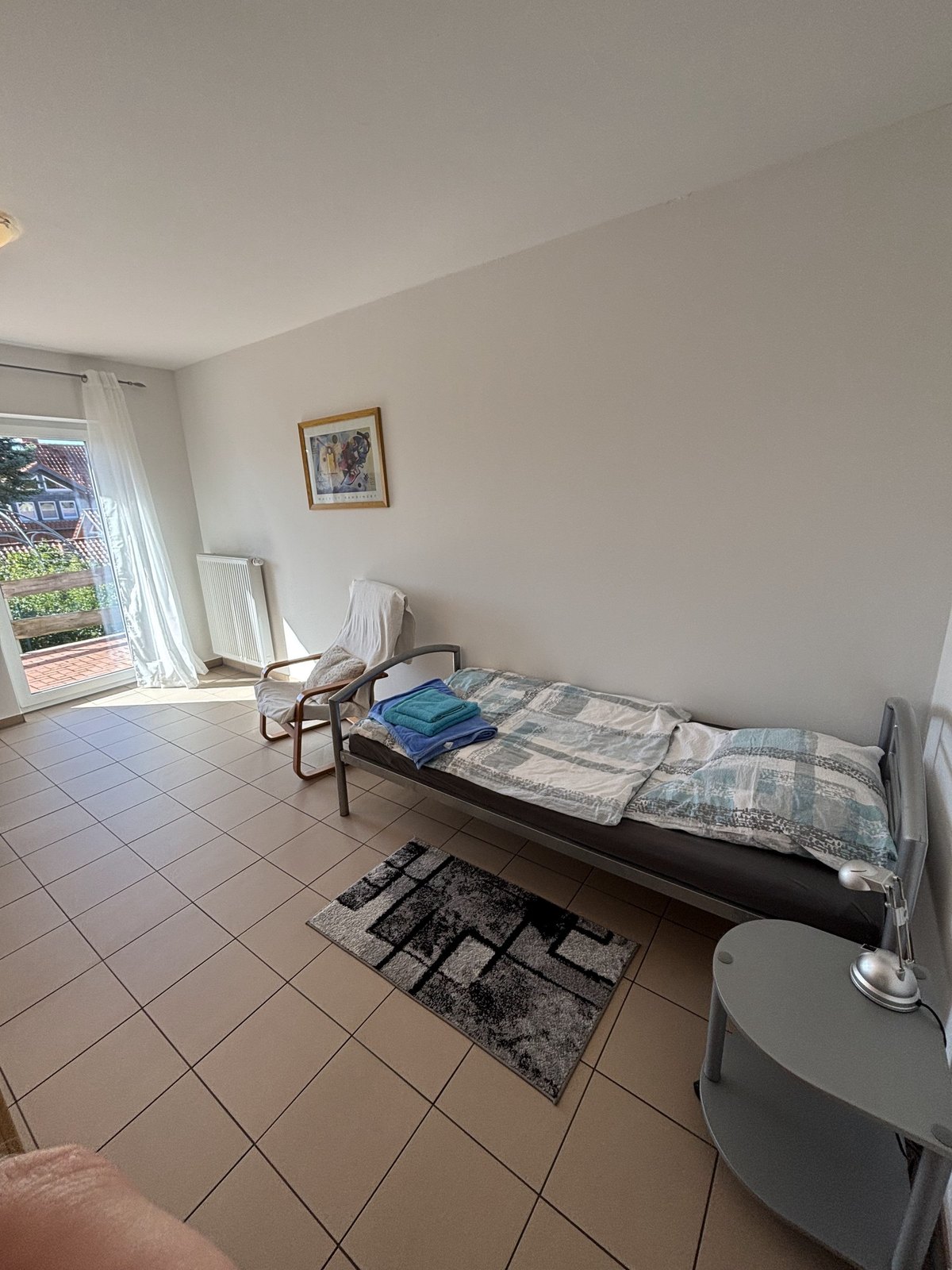 Einzelzimmer mit Bett, Sessel und Zugang zum Balkon