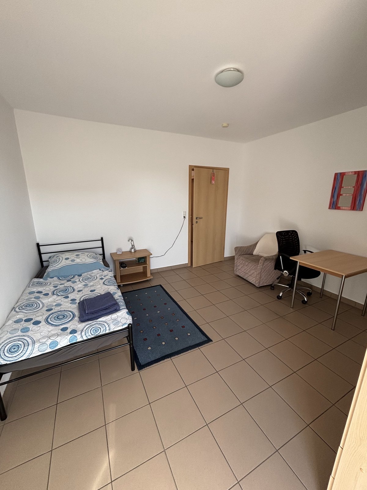 Einzelzimmer mit Bett, Schreibtisch und Sessel